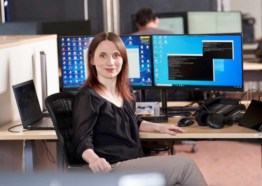 IT-Mitarbeiterin Frau Stolz. Im Hintergrund befinden sich zwei PC Monitore.