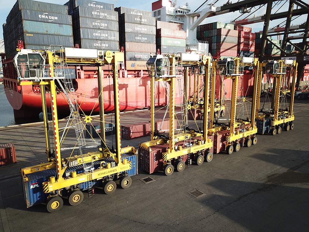 Vier Konecranes Noell Straddle Carrier nebeneinander. Dahinter sind viele Container.